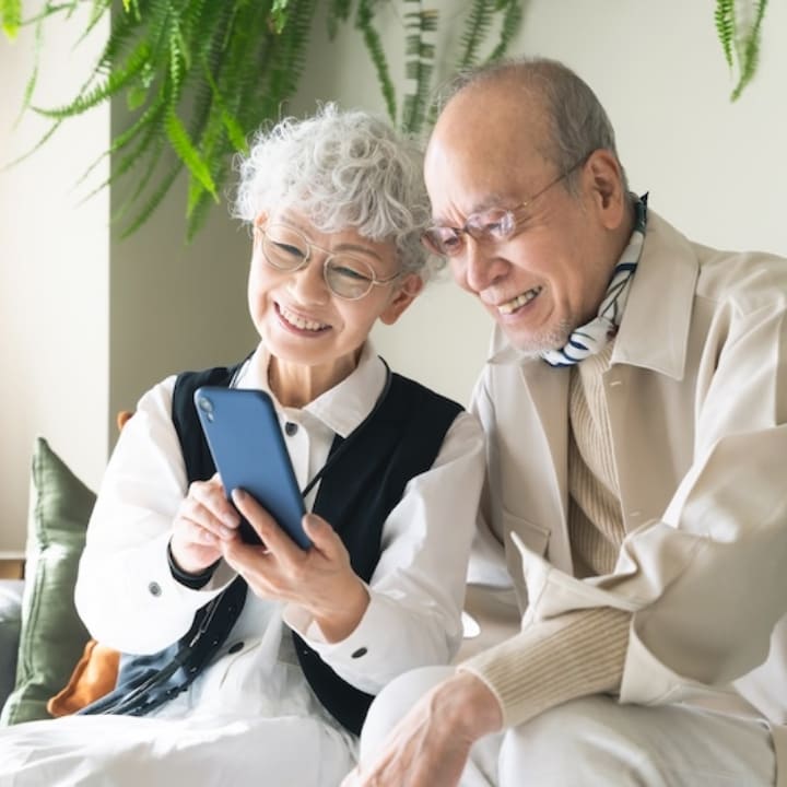 外国人や高齢者へのサポートを表現する、スマートフォンを見る笑顔の高齢夫婦